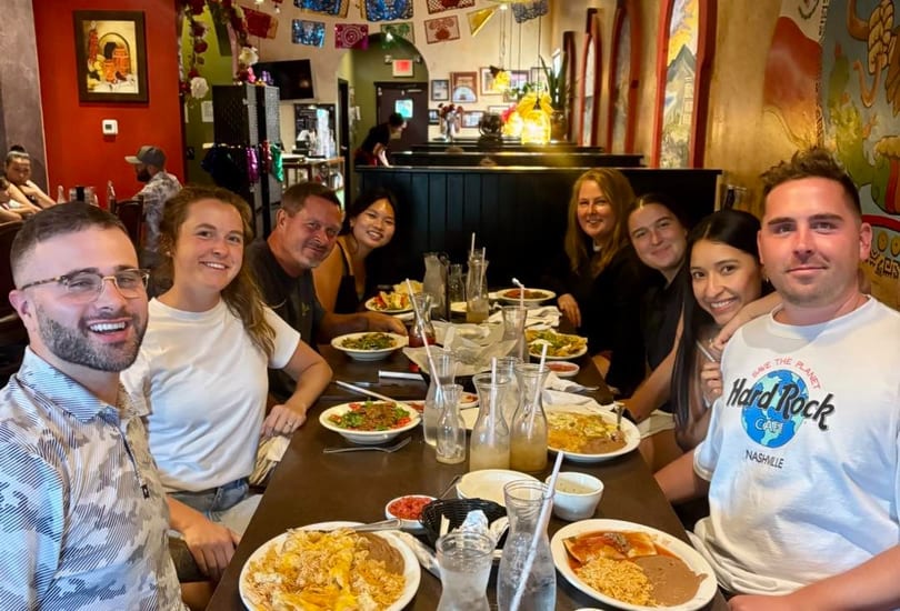 Group of eight smiling people dining at a long table filled with Mexican food and drinks.